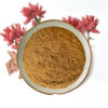 Overhead presentation of Rhodiola rosea root extract powder in a ceramic dish surrounded by red flowers and reddish-brown woody fragments