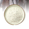 Off-white vanilla powder piled in a shallow ceramic plate with dark vanilla pods arranged in the background.